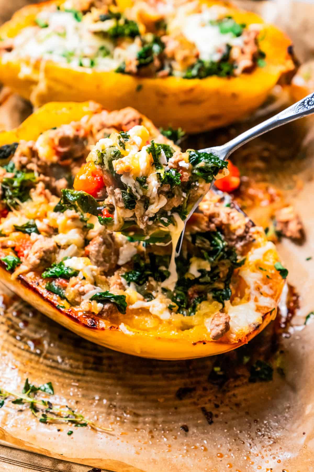 A fork lifting Mediterranean-inspired turkey filling from a spaghetti squash boat, with a second squash in the background.