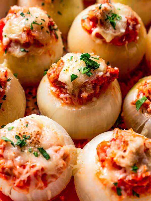 Close up of sausage stuffed onions in rows inside a baking dish.