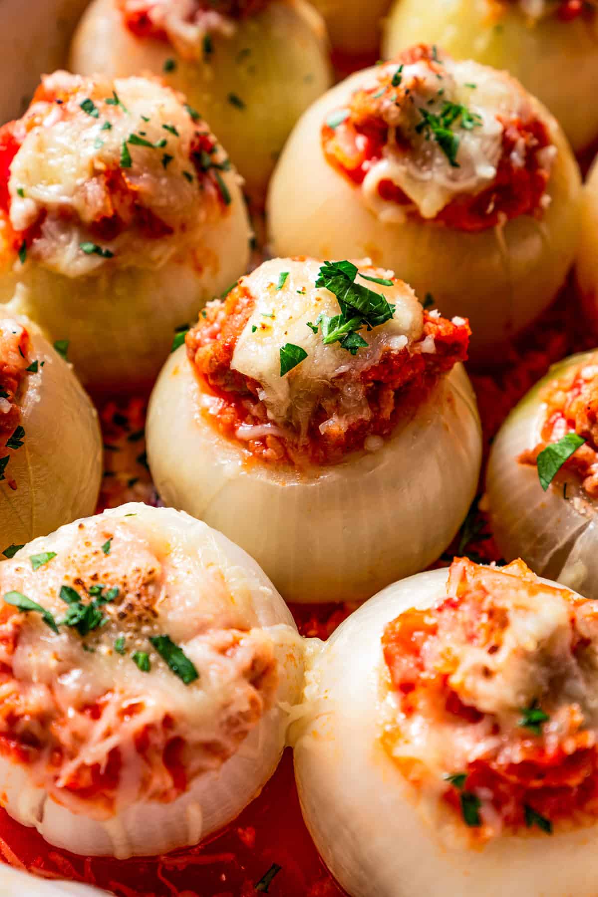 Close up of sausage stuffed onions in rows inside a baking dish.