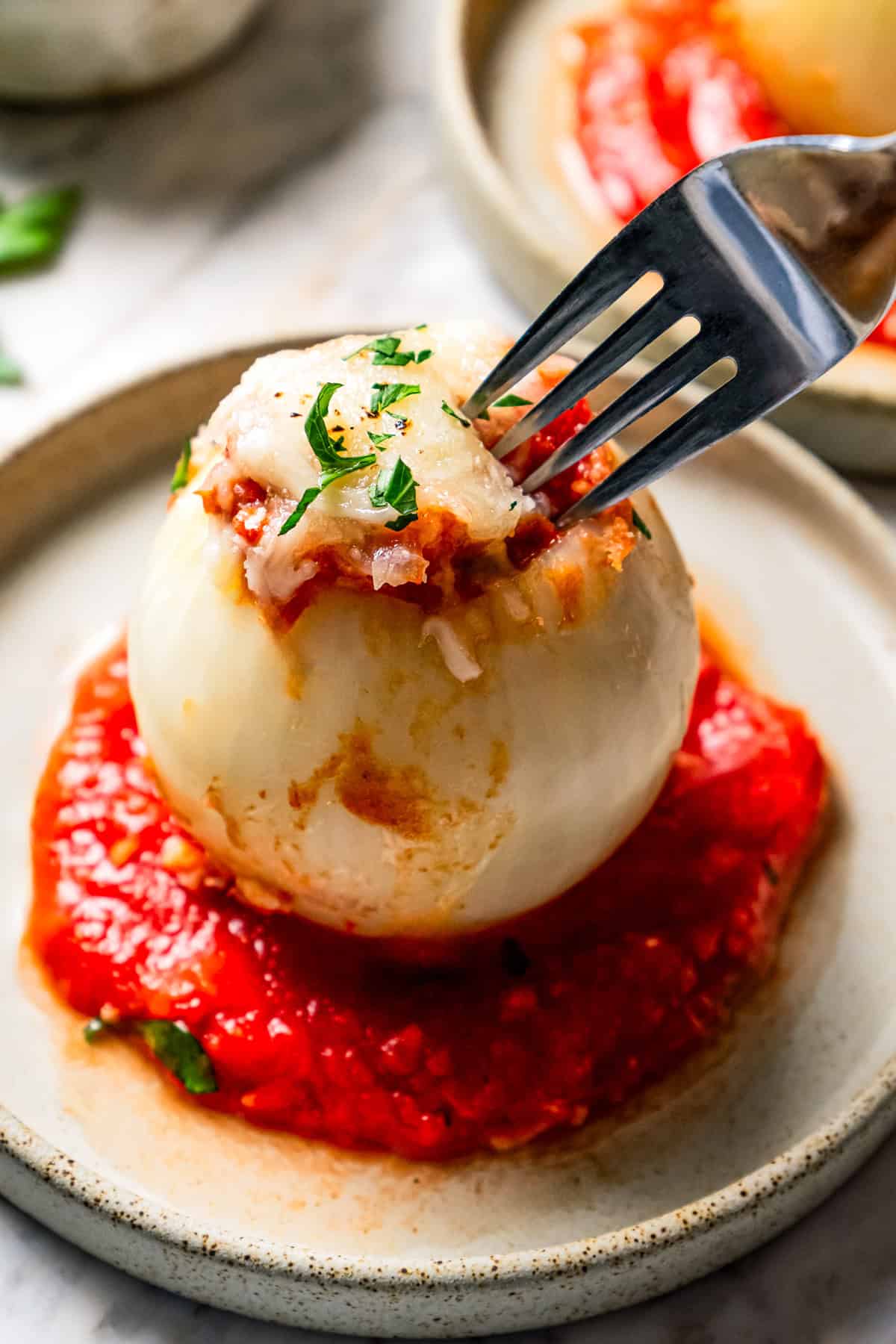 A fork poking into a stuffed onion served over a bed of tomato sauce on a stoneware plate.