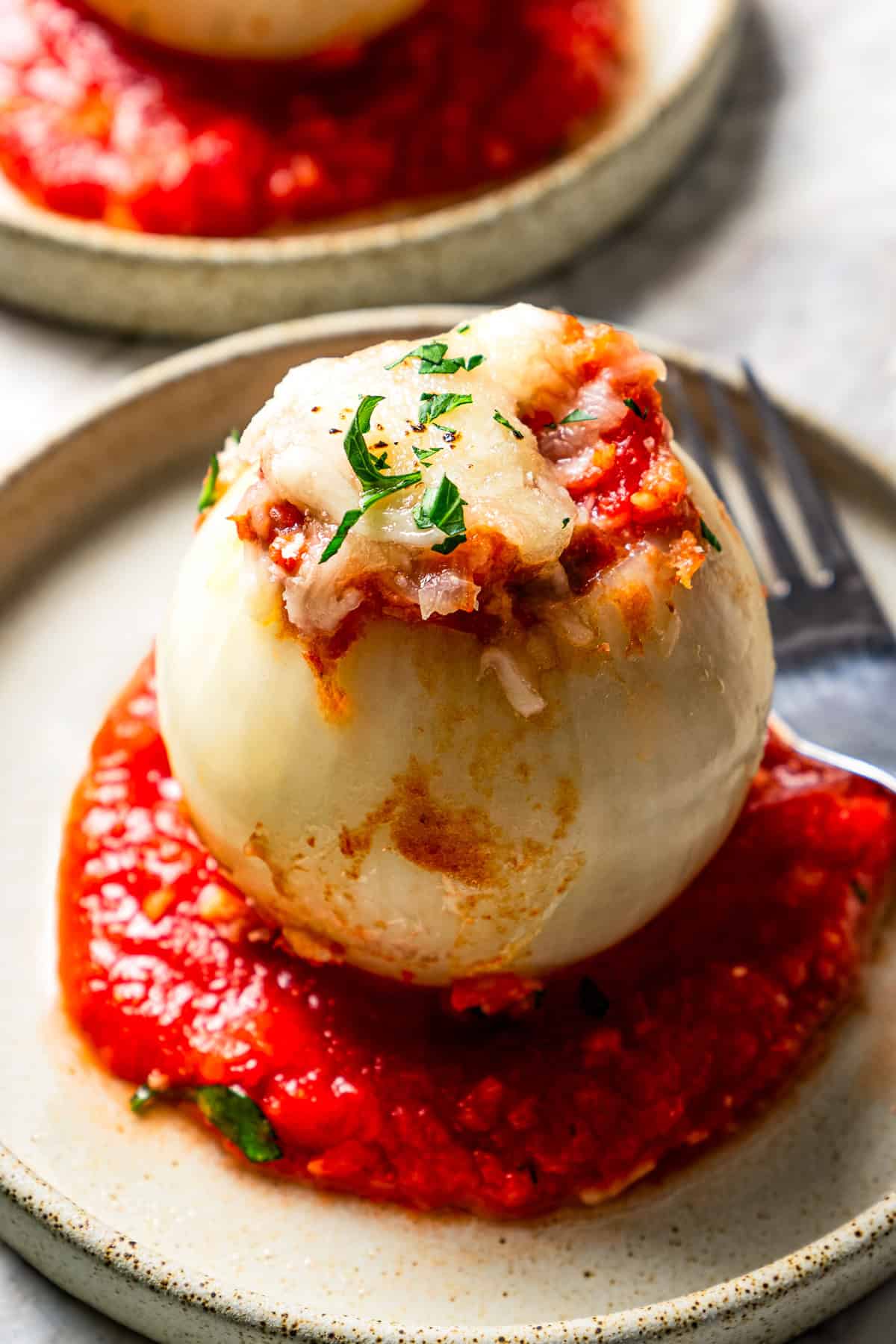 A stuffed onion served over tomato sauce on a dinner plate next to another plate.