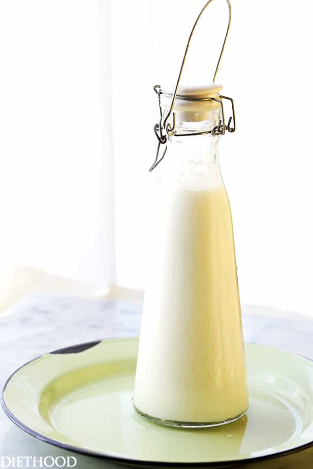 Side view of homemade buttermilk in a glass bottle with a clip-top lid, on a green plate.