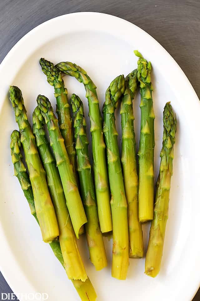 Asparagus spears are steamed and arranged on a white plate.
