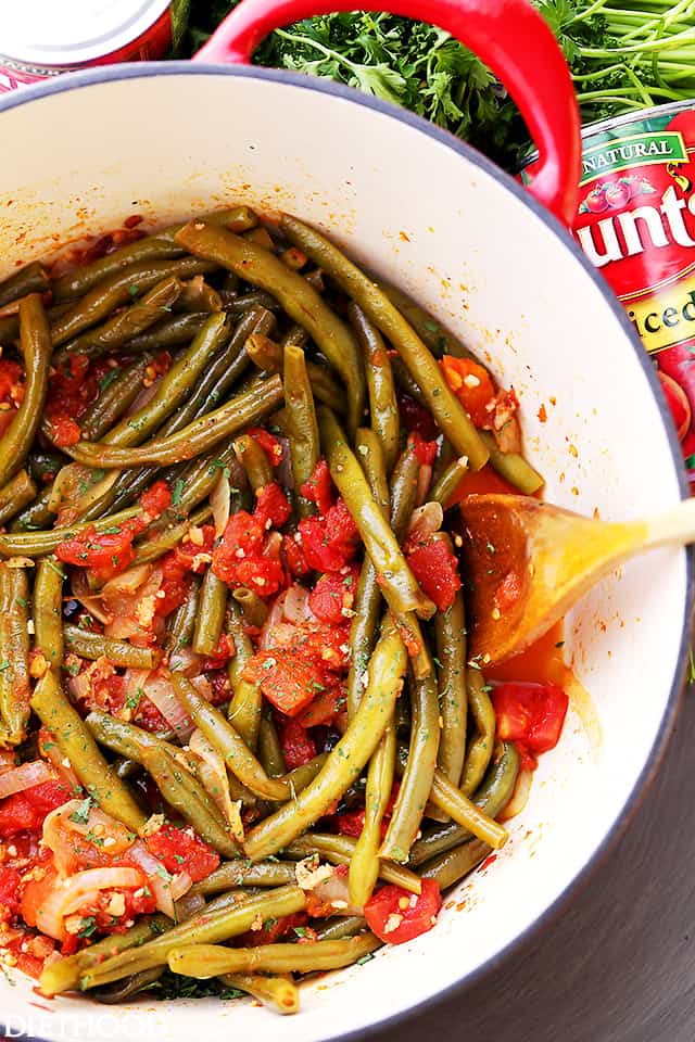 Green Beans and Tomatoes mixed together in a pot with a wooden spoon