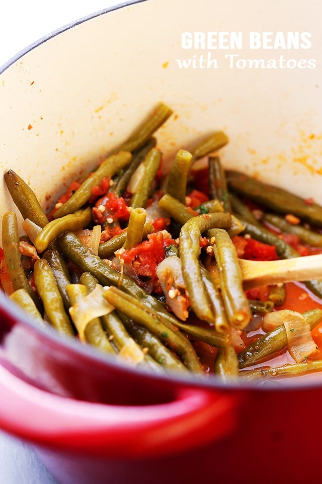 Green Beans and Tomatoes in a red pot being stirred with spoon