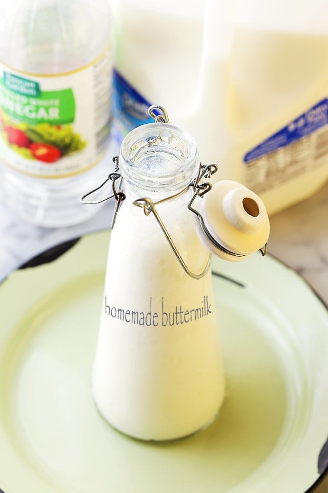 Homemade buttermilk in a glass milk bottle with a clip-top lid, with a bag of milk and bottle of vinegar in the background.