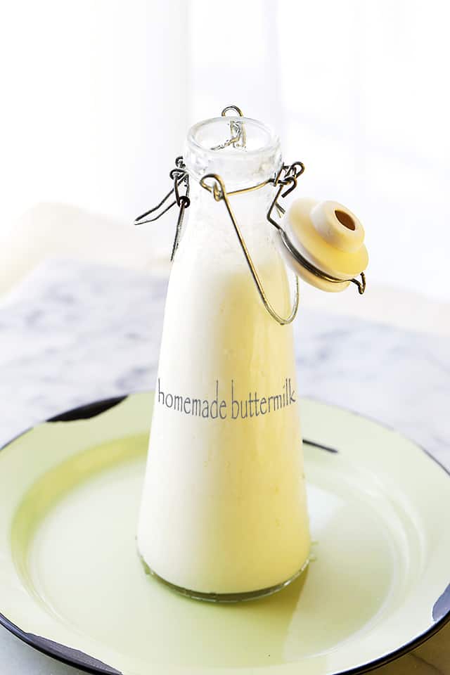 Homemade buttermilk in a glass bottle with a clip-top lid, on a plate.