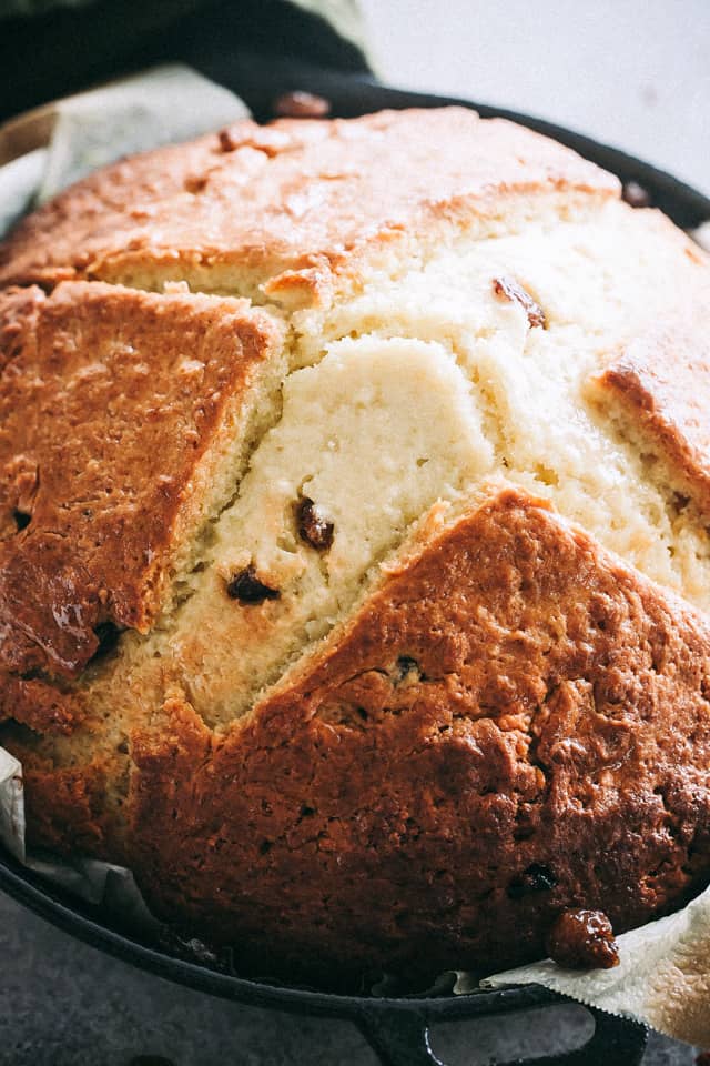 A loaf of Irish soda bread in a parchment-lined cast iron skillet.