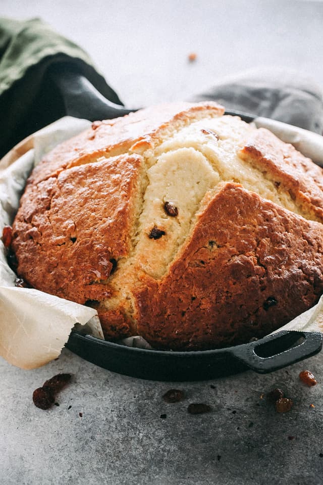 A loaf of Irish soda bread in a parchment-lined cast iron skillet.