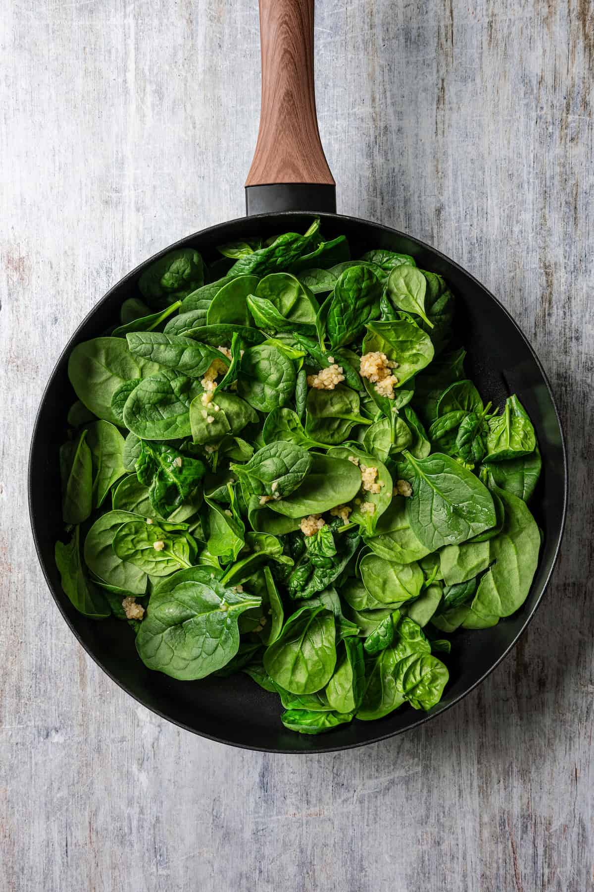 Fresh spinach and minced garlic added to a skillet.