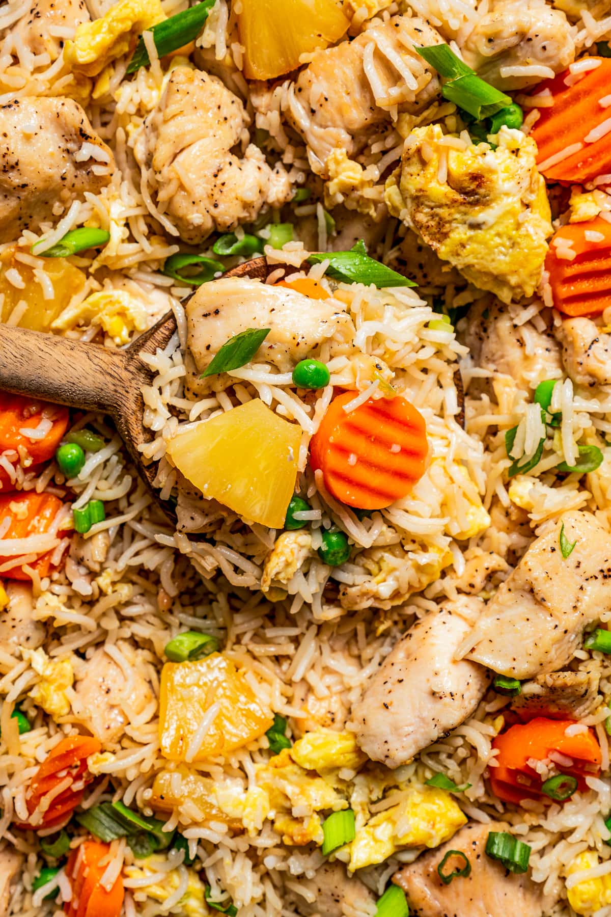 Up close image of a wooden spoon scooping out fried rice with chicken.