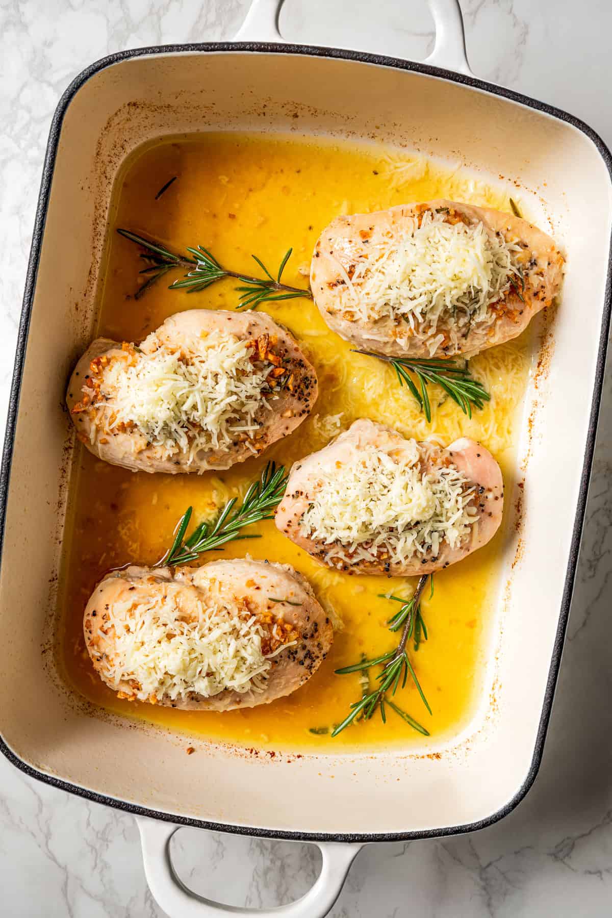 Baked chicken breasts topped with melted cheese in a ceramic baking dish.