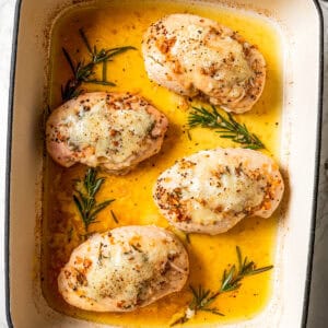 Four baked chicken breasts in a baking dish.