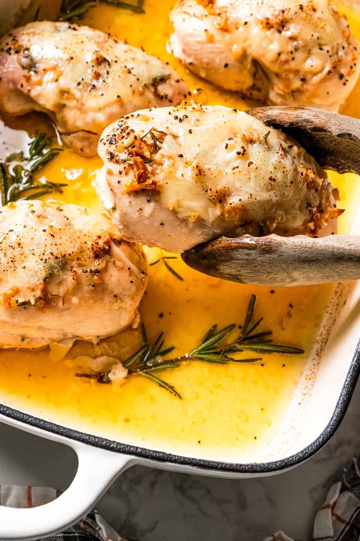 A pair of tongs lifting a chicken breast from a baking dish.