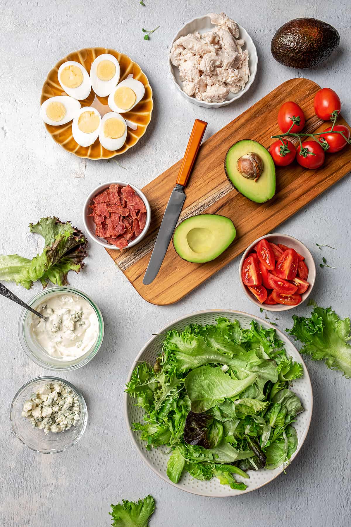 Overhead view of various Cobb salad ingredients arranged around a bowl of mixed greens.
