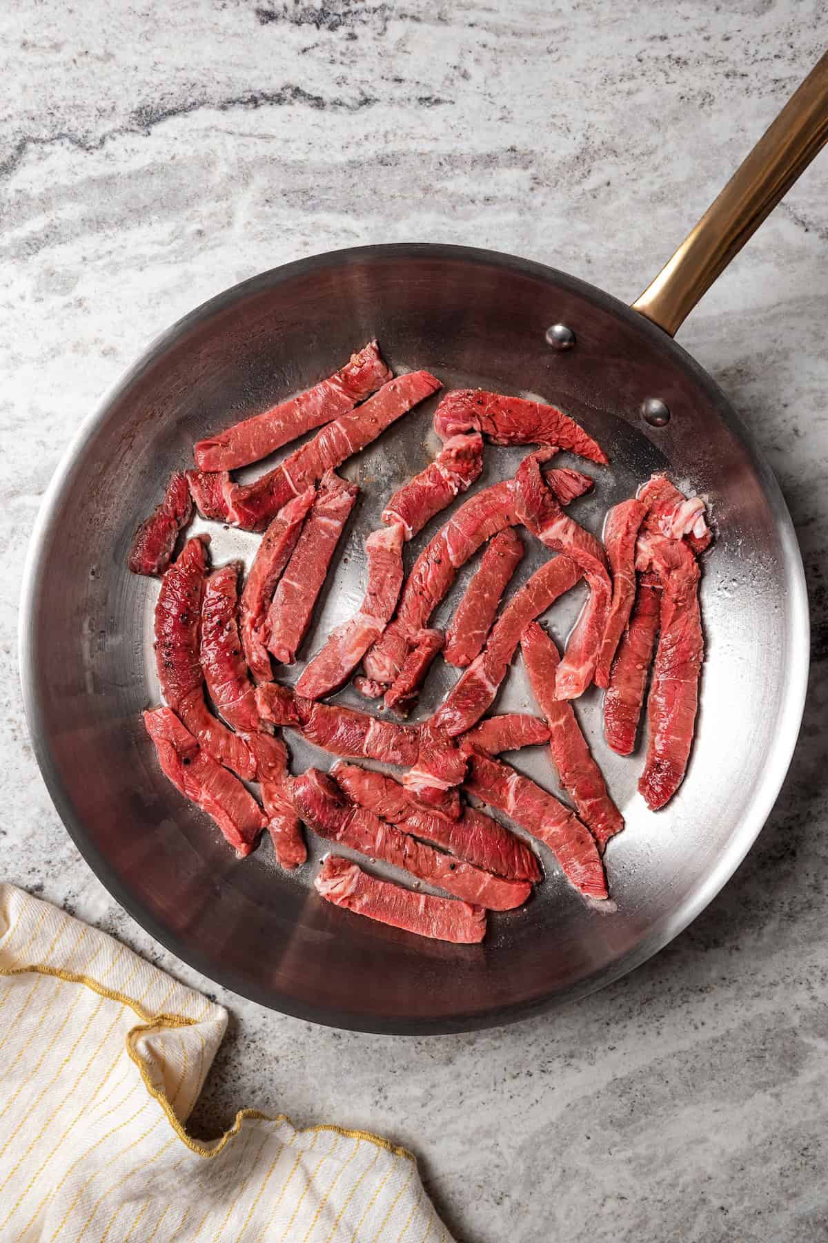 Beef strips added to a skillet.