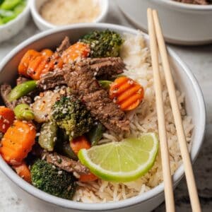 Ginger beef stir fry served over a bowl of rice with a set of chopsticks.