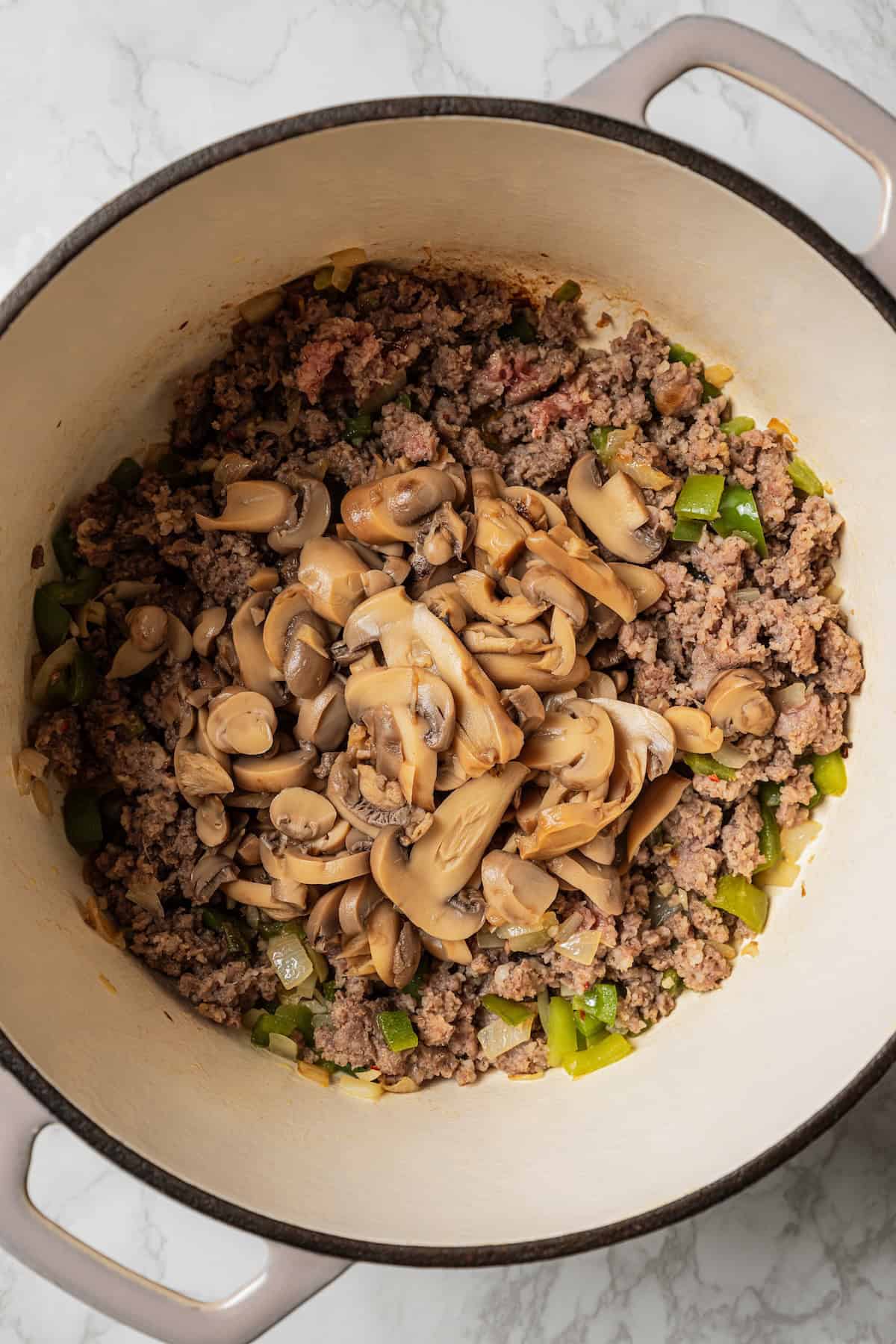 Cooked sausage, mushrooms, and peppers in a large pot.