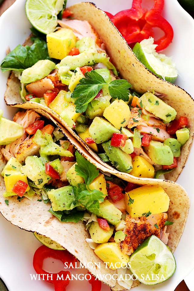 Fresh fish tacos with avocado and mango topping, in soft taco shells on a white platter.