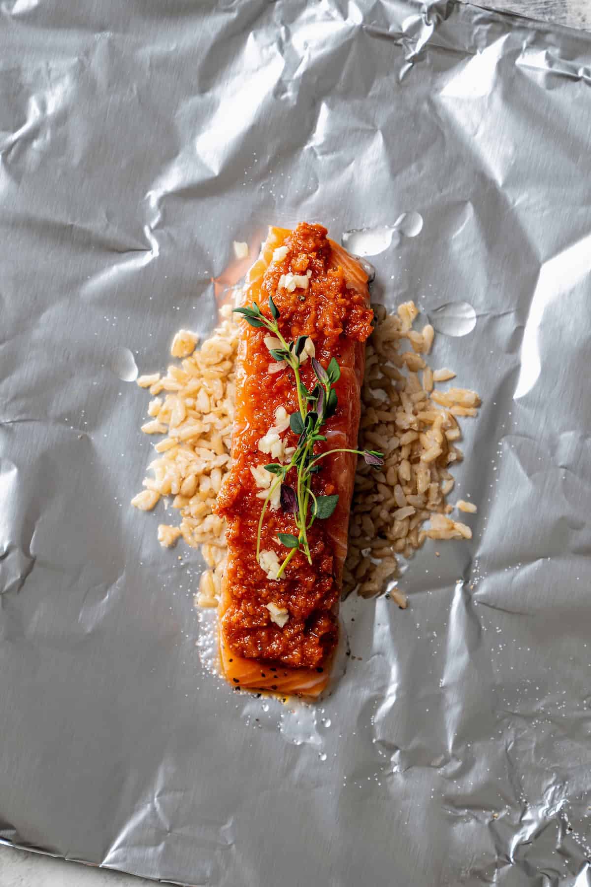 Rice topped with a salmon filet and tomato pesto on a sheet of foil.