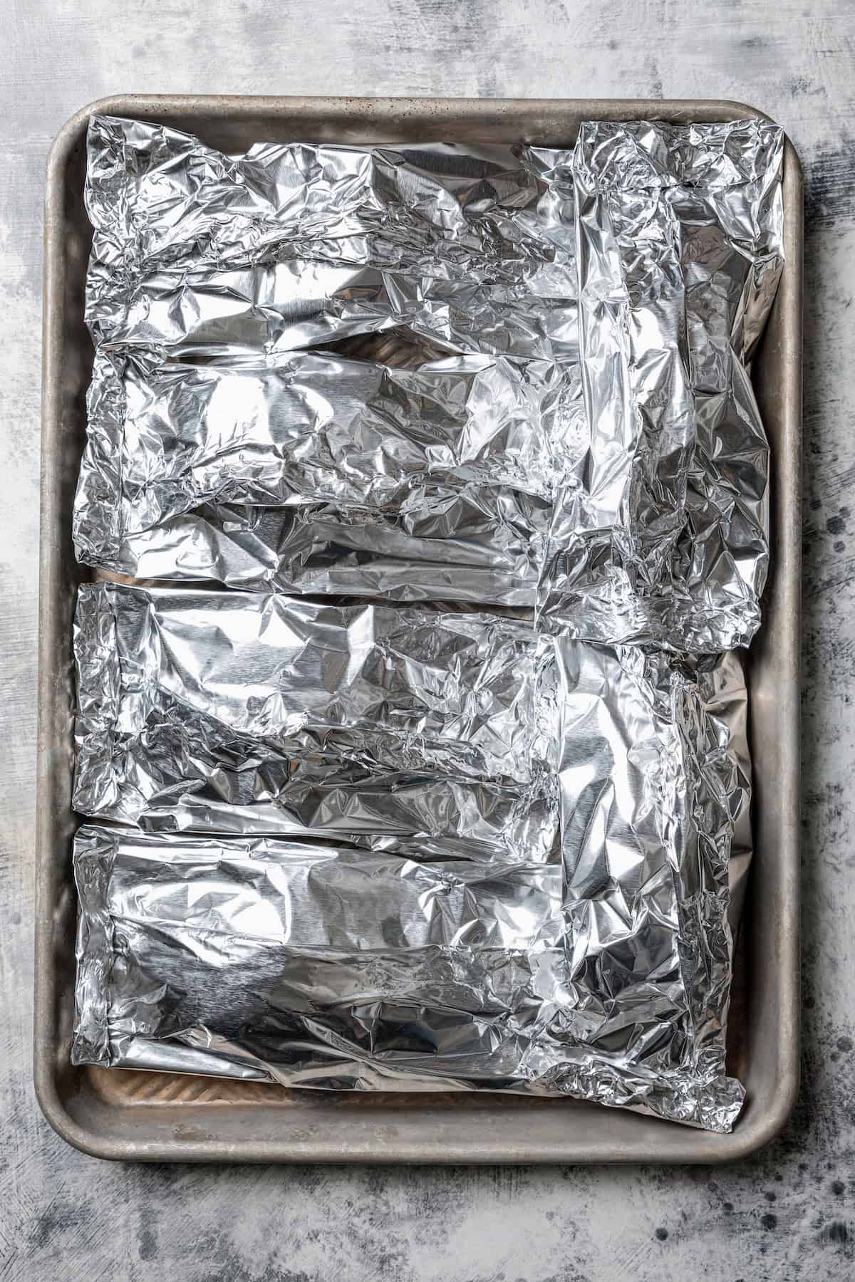 Sealed salmon and rice foil packets on a baking sheet.