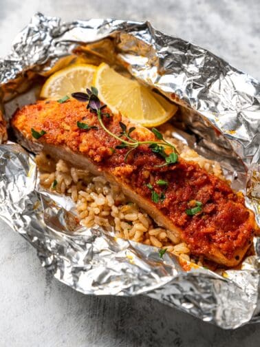 Salmon and rice in an open foil packet garnished with lemon wedges.