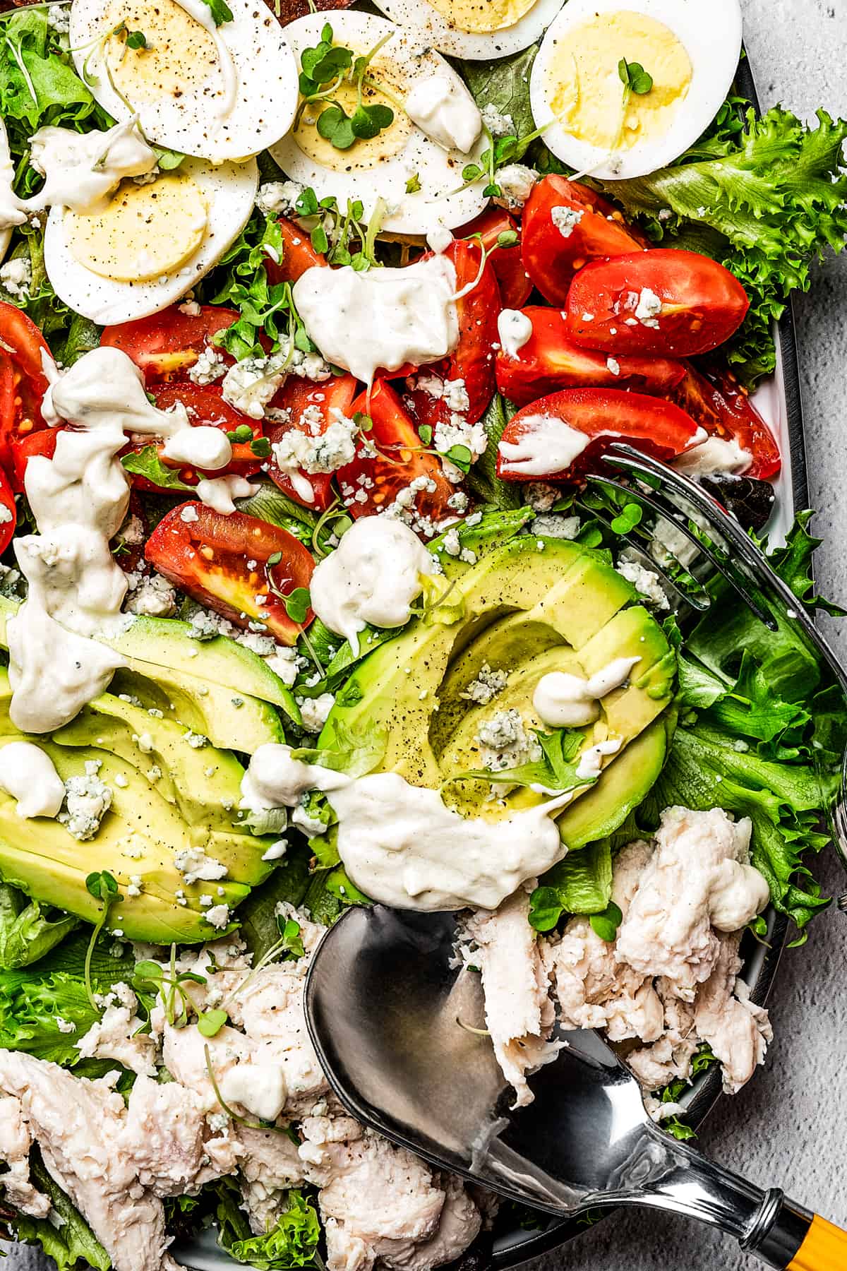 Close up of Cobb salad on a platter topped with blue cheese dressing.