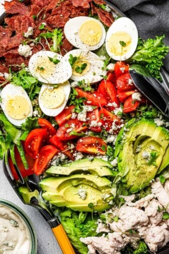 overhead shot of a plate with Cobb salad topped with avocados, tomatoes, eggs, and chicken and drizzled with blue cheese dressing.