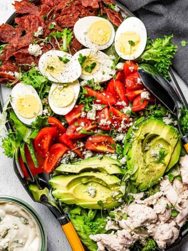 overhead shot of a plate with Cobb salad topped with avocados, tomatoes, eggs, and chicken and drizzled with blue cheese dressing.