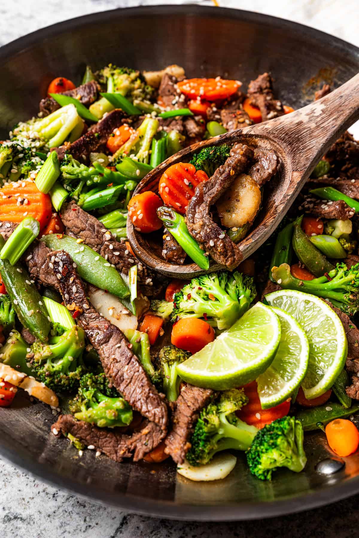 Overhead view of ginger beef stir fry in a large metal skillet with a wooden spoon.