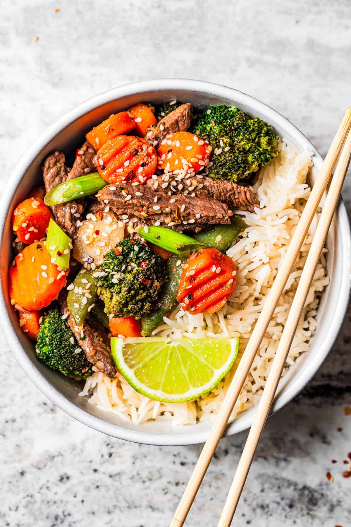 Beef stir fry and vegetables served with rice in a bowl, with chopsticks resting on the side of the bowl.