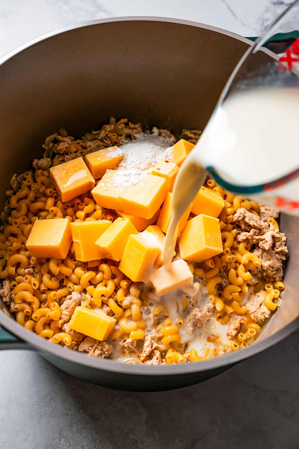 Cheese cubes and milk added to a pot of cooked elbow macaroni pasta.