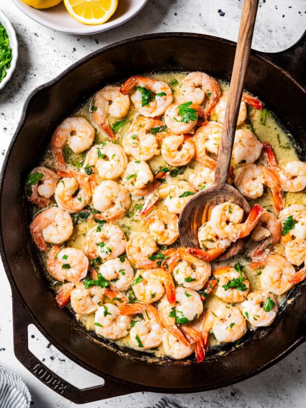 Overhead view of lemon garlic shrimp in a skillet with a wooden spoon.