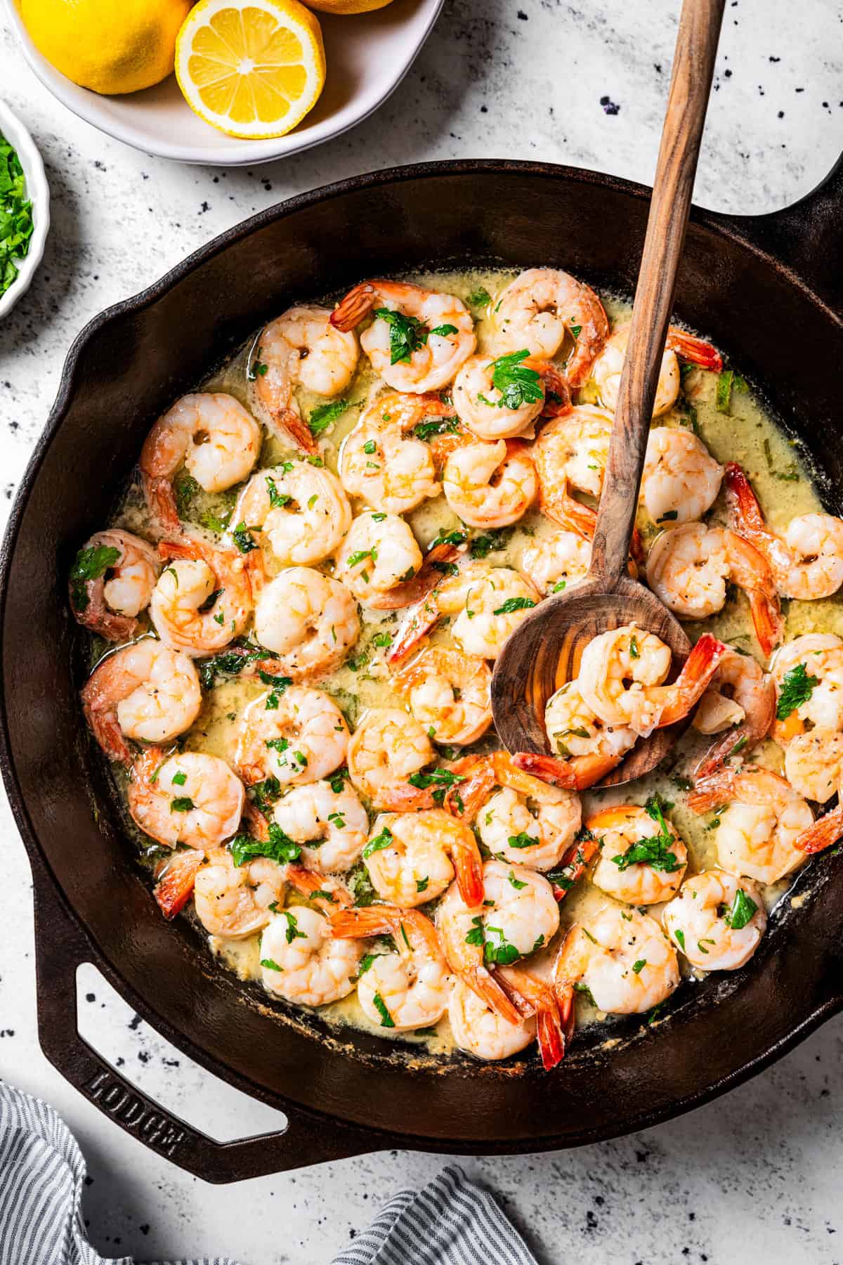 Overhead view of lemon garlic shrimp in a skillet with a wooden spoon.