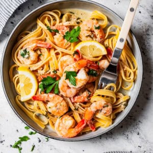 Overhead view of lemon garlic shrimp served over a bowl of pasta garnished with parsley and a lemon wedge.