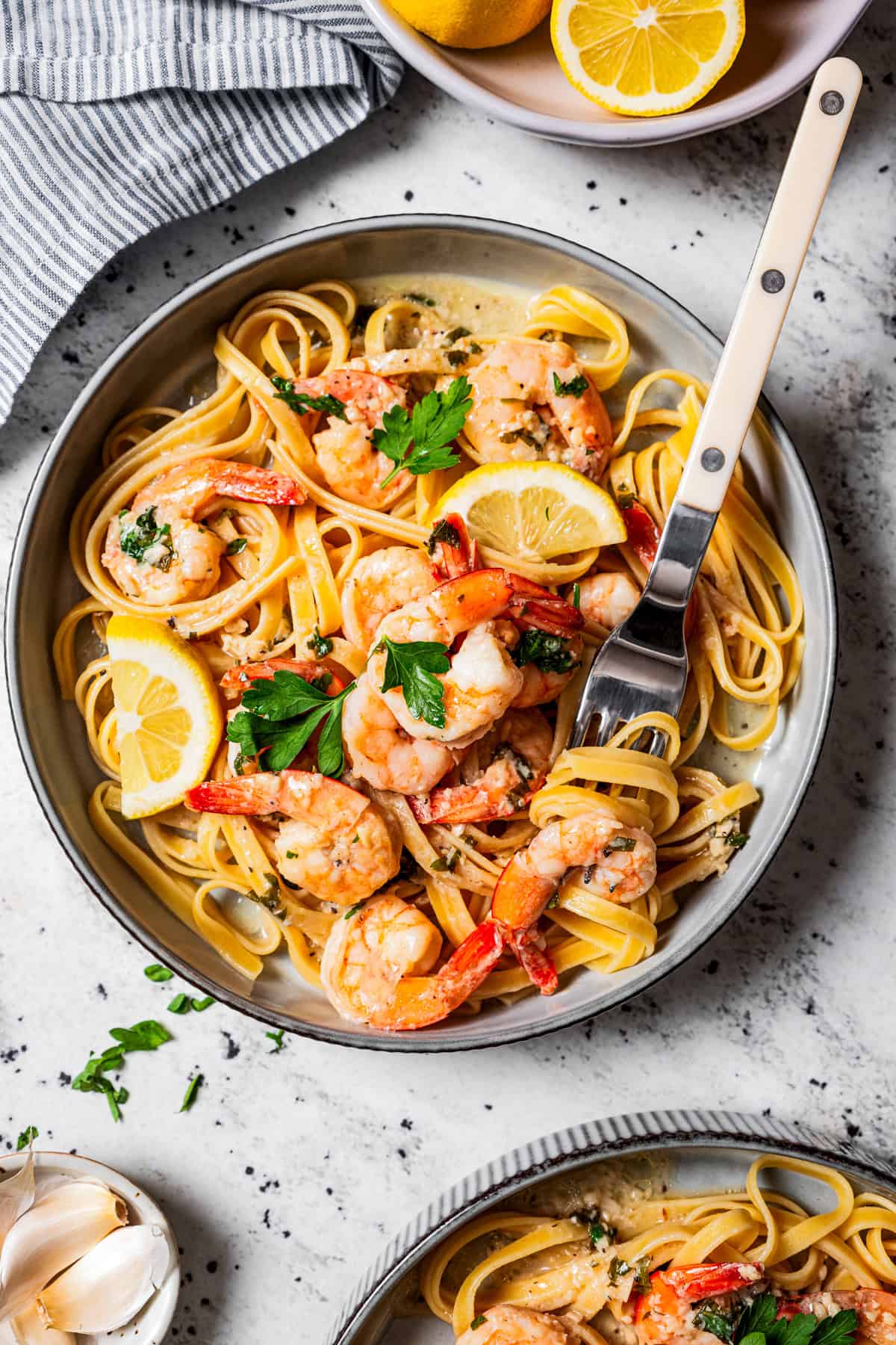 Overhead view of lemon garlic shrimp served over a bowl of pasta garnished with parsley and a lemon wedge.