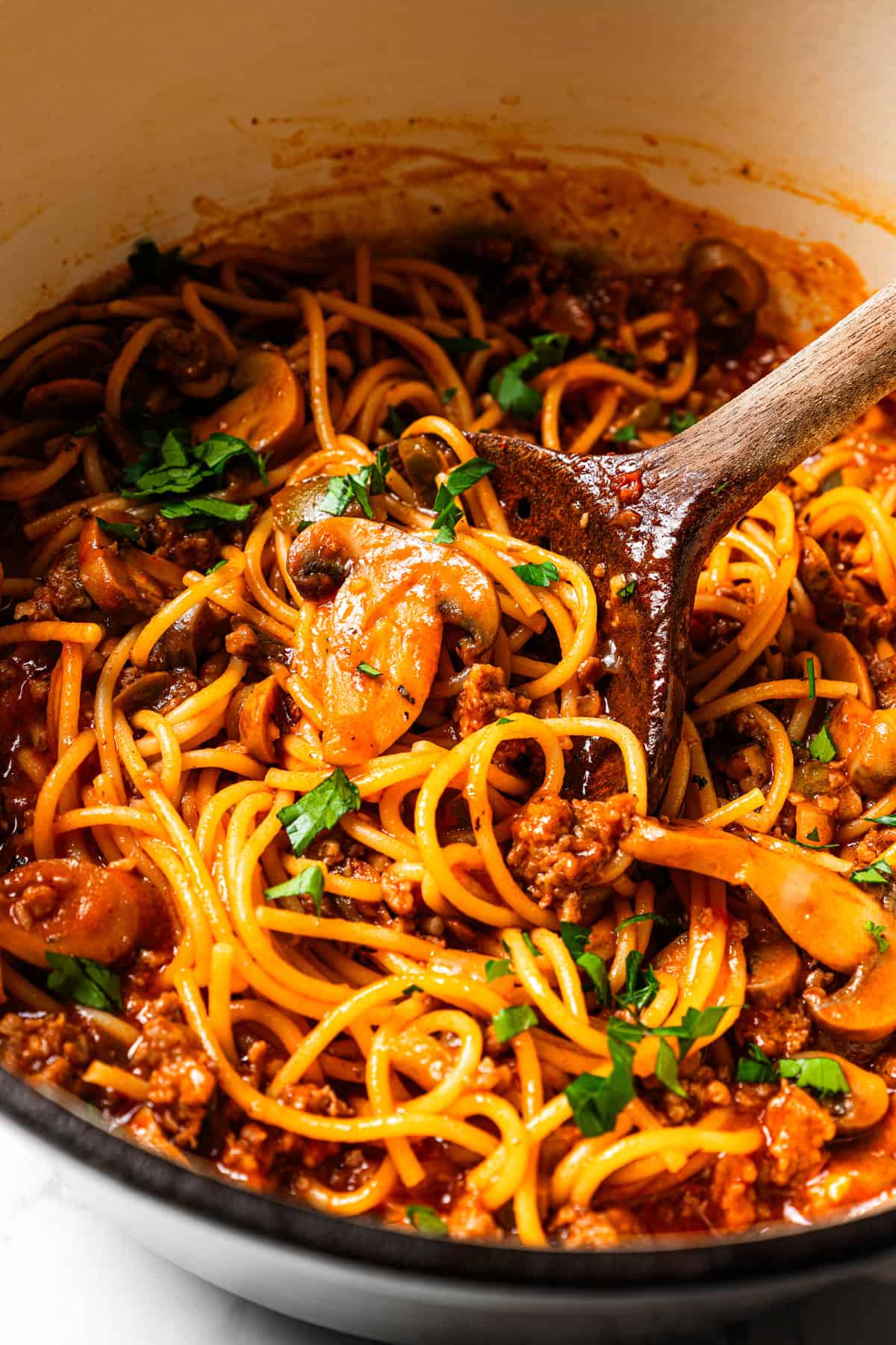 A wooden spoon stirring through spaghetti in a pot.