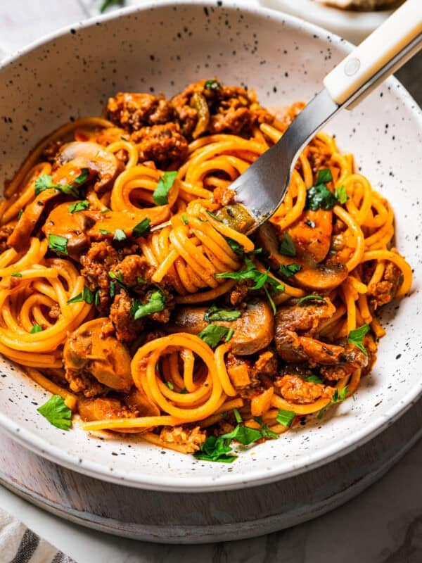 A fork picking up a bite of sausage and spaghetti from a bowl.