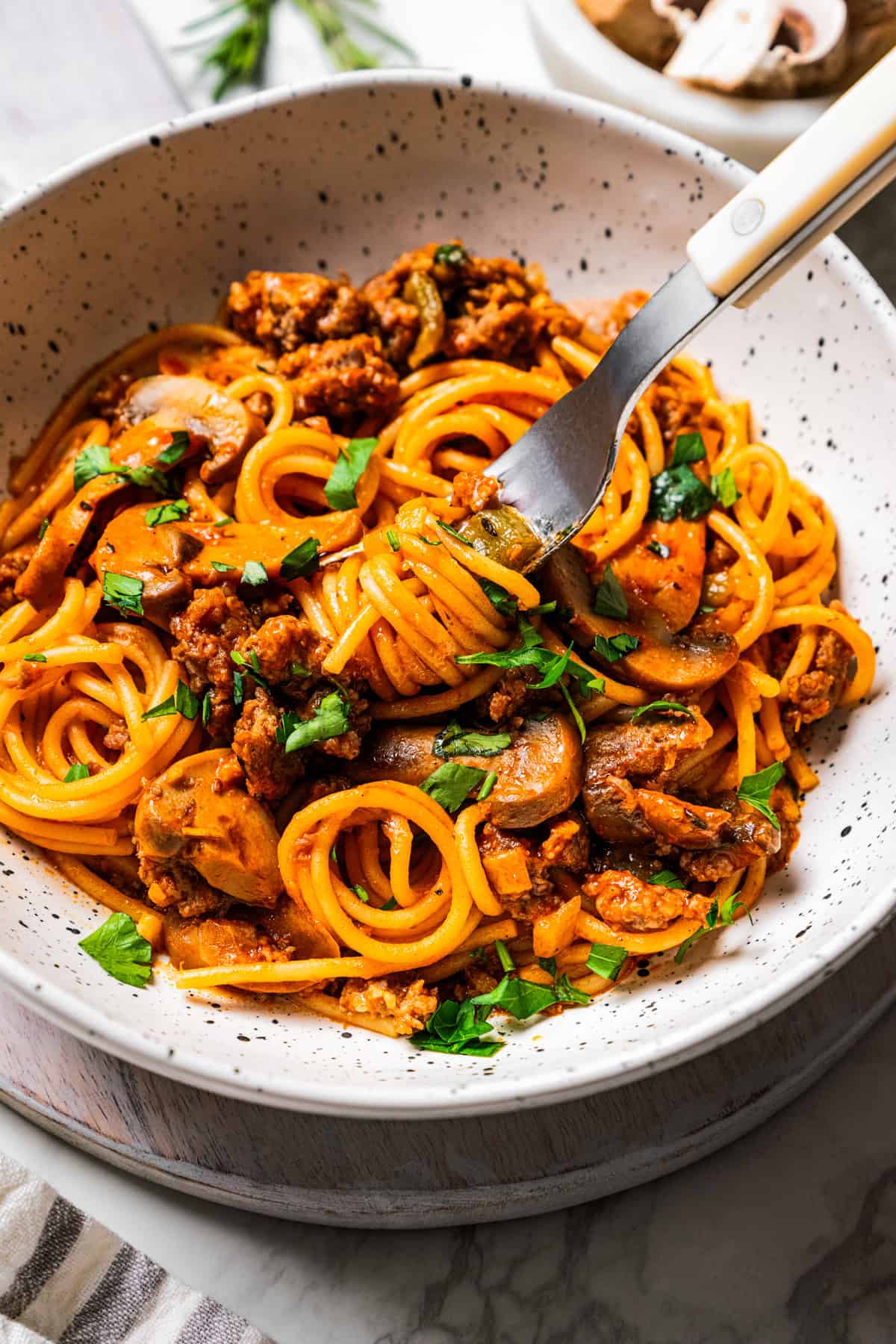 A fork picking up a bite of sausage and spaghetti from a bowl.