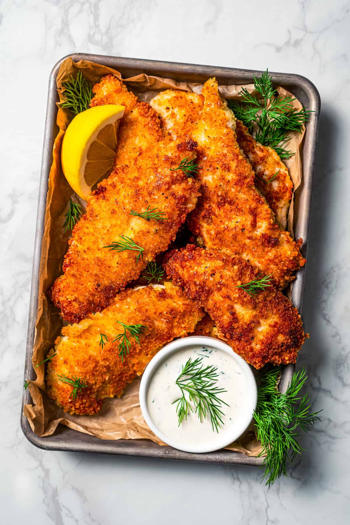 Chicken tenders garnished with lemon wedges on a tray next to a small bowl of buttermilk ranch dressing.