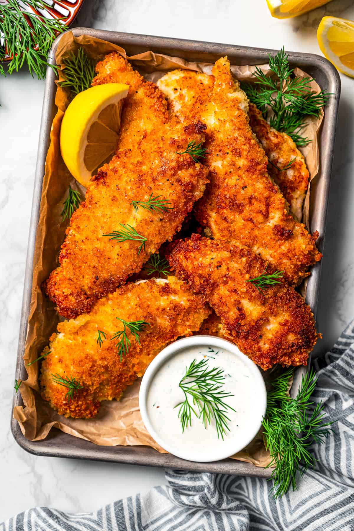 Overhead view of parmesan chicken tenders garnished with lemon wedges on a tray next to a small bowl of buttermilk ranch dressing.