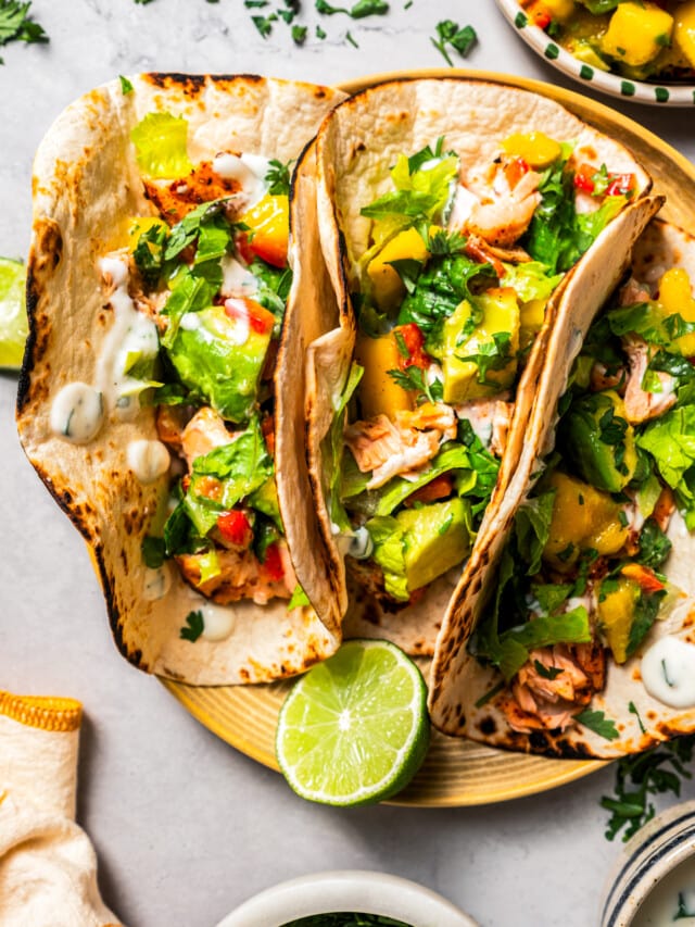 Overhead of three salmon tacos with mango avocado salsa served on a plate.