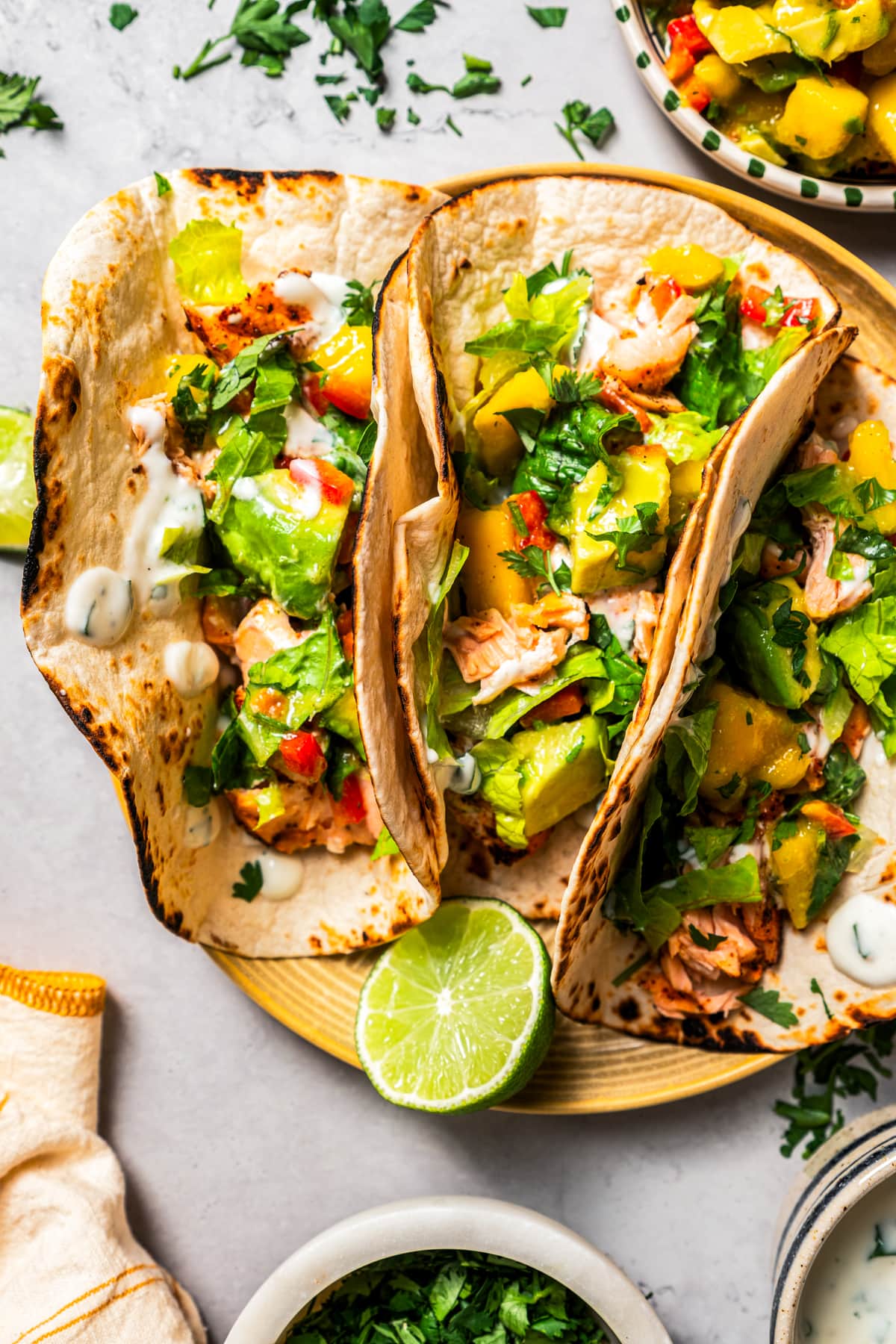 Overhead of three salmon tacos with mango avocado salsa served on a plate.