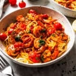 Spicy shrimp fra diavolo served over a bowl of spaghetti, with a second bowl of pasta in the background.