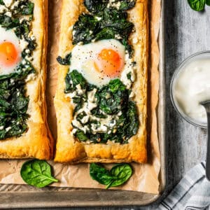 Overhead view of two spinach and feta puff pastries served on a parchment-lined baking sheet.