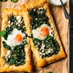 Overhead view of two puff pastries topped with spinach, feta, and an egg yolk.