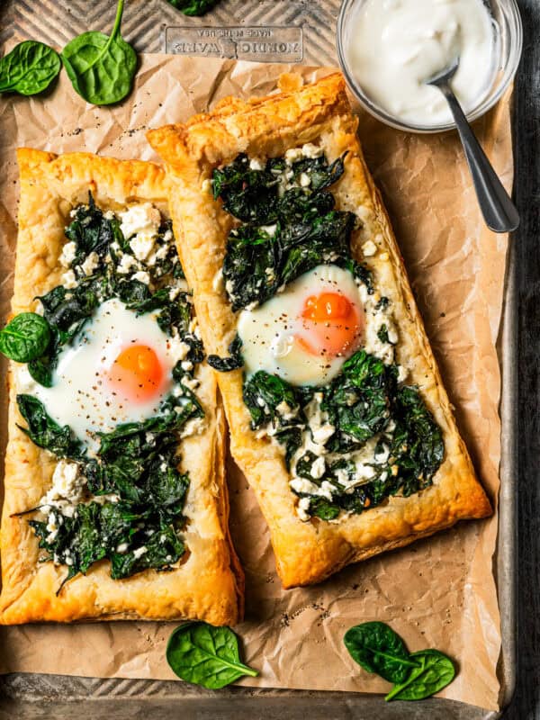 Overhead view of two puff pastries topped with spinach, feta, and an egg yolk.