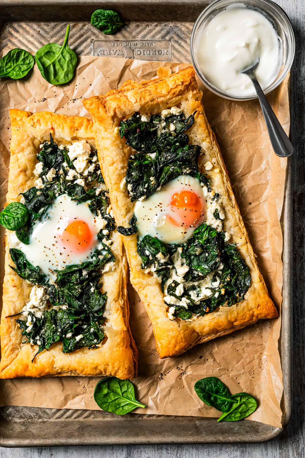 Overhead view of two puff pastries topped with spinach, feta, and an egg yolk.