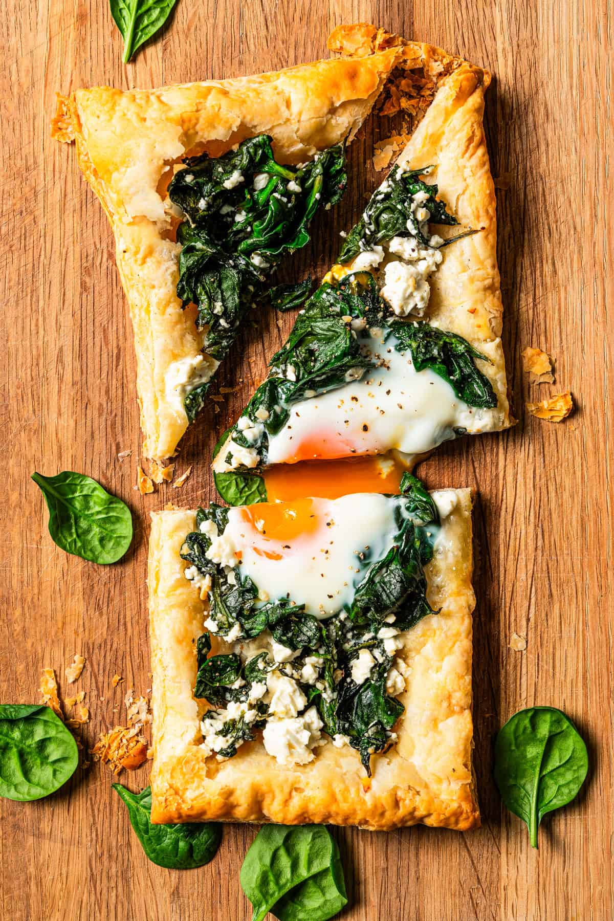 Spinach and feta pastry cut in half, with one half cut into triangles on a wooden cutting board.