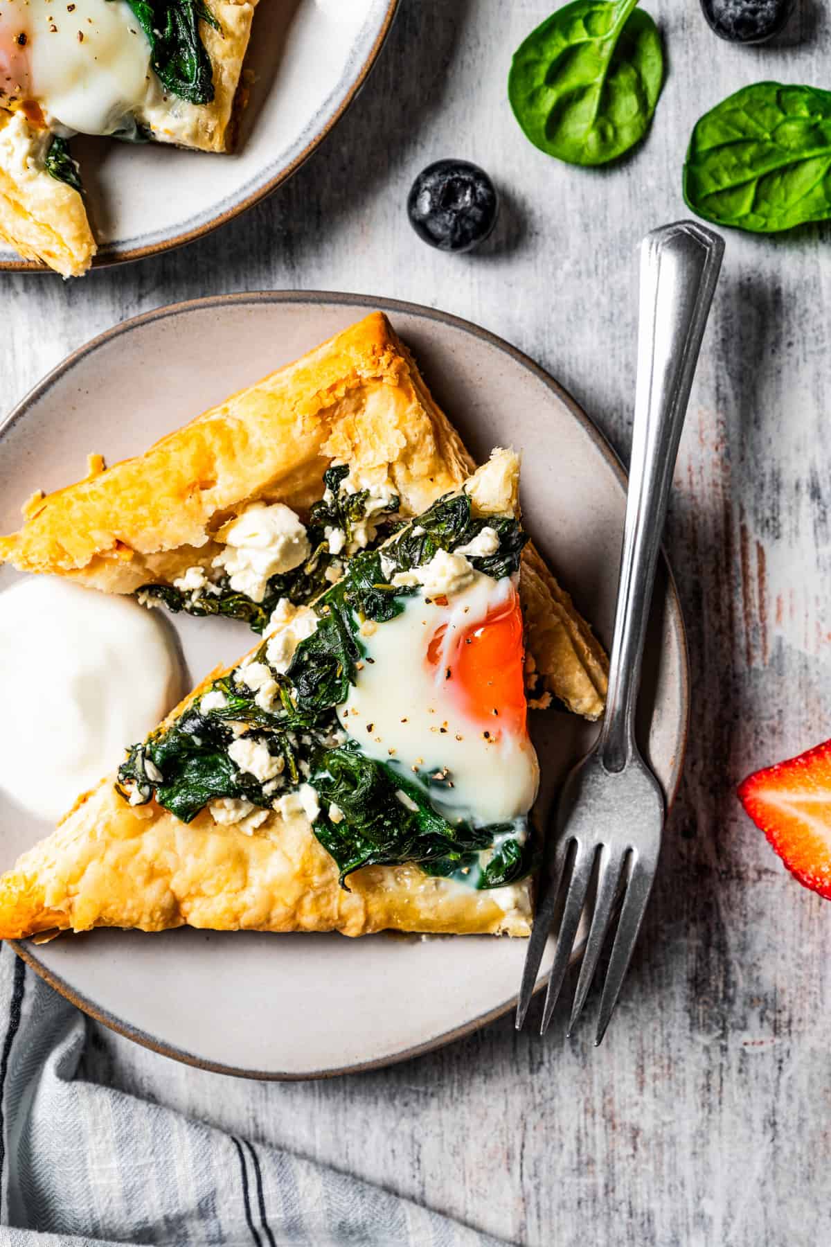 Puff pastry triangles topped with spinach, feta, and egg, and served on a plate with a fork next to it.